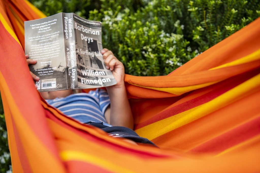 Hombre sentado en hamaca, leyendo libro de surf