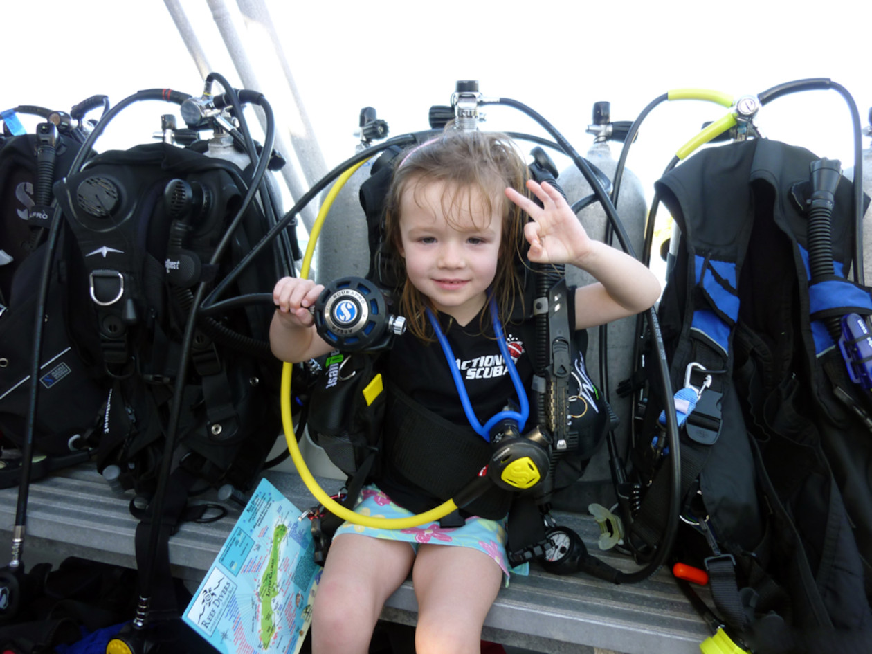 Niña pequeña vistiendo el equipo de buceo, haciendo señas con las manos